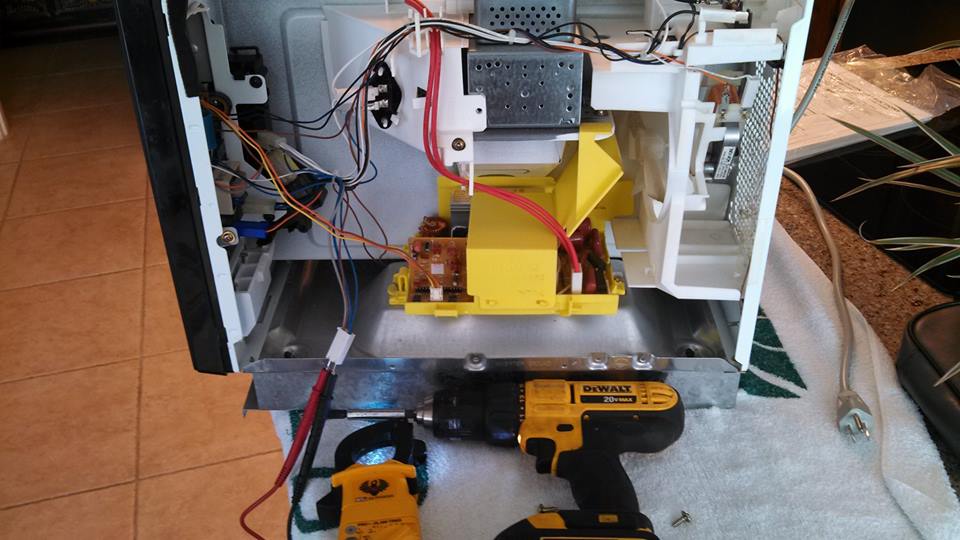 A microwave opened up for repair with a meter and drill beside it